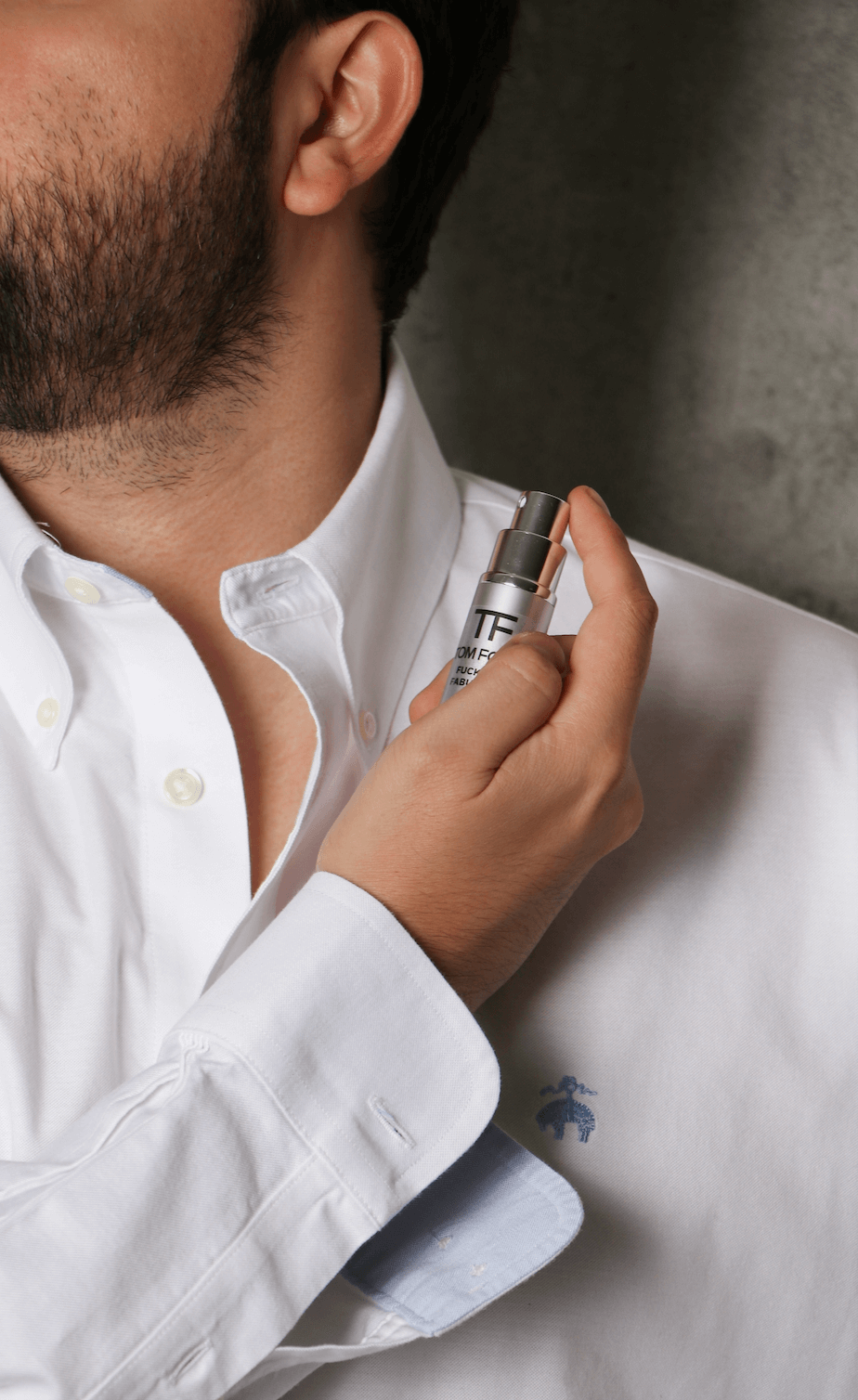 Hombre aplicándose perfume en el cuello, usando camisa blanca. Decant.