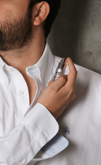Hombre aplicándose perfume en el cuello, usando camisa blanca. Decant.