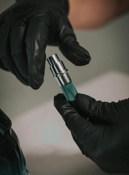 Persona con guantes negros sostenido un frasco de vidrio con líquido azul para el proceso de Decant